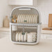 Two tier dish rack with enclosed storage on kitchen countertop showing plates, bowls, cups and glasses